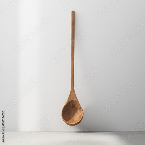 Long wooden spoon hanging on a white wall, well-lit minimalistic kitchen accessory, ideal for cooking and serving. photo