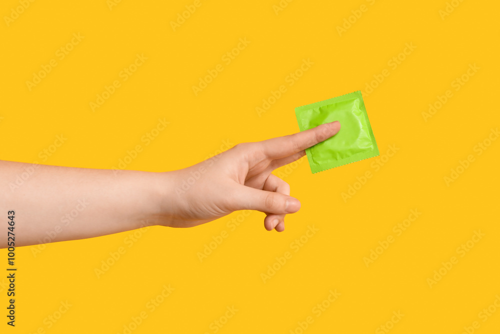 Female hand with condom on yellow background, closeup Female hand with condom on yellow background, closeup