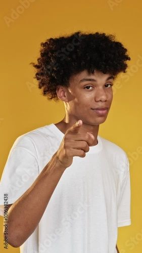 Vertical video. Heart gesture. Love sign. Confident guy flirting blowing air kiss expressing adore romantic affection isolated on yellow background.