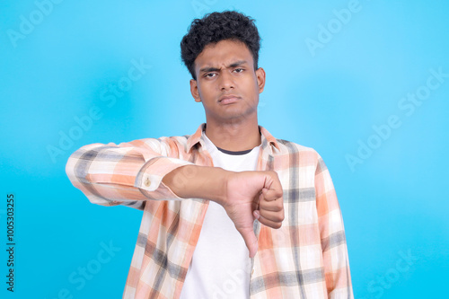Canvas Print Upset Young Asian Man in Casual Clothes Showing Thumb Down Isolated on Blue Back