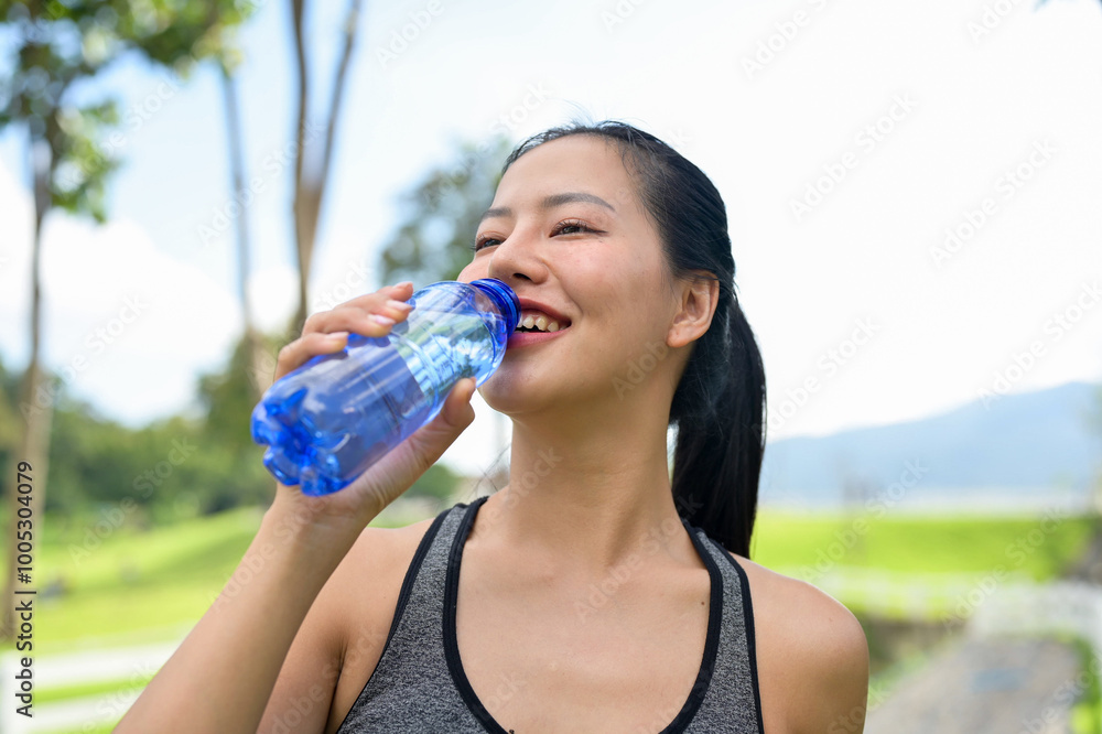 A fit woman in sportswear drinks from a water bottle, quenching her thirst after jogging in a park. A fit woman in sportswear drinks from a water bottle, quenching her thirst after jogging in a park.