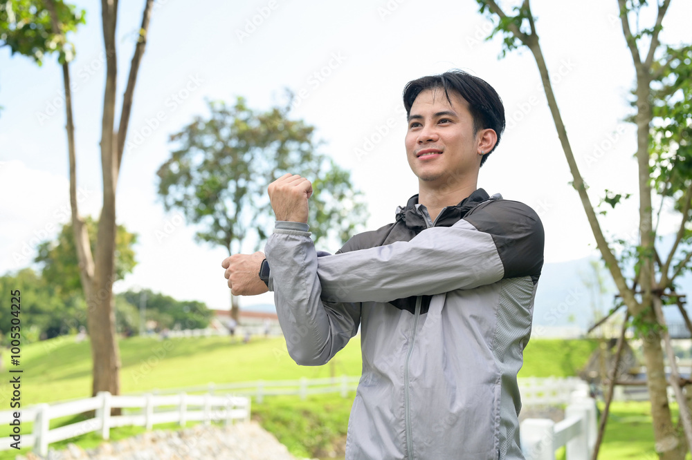 A handsome, fit Asian man in sportswear stretches his arm, warming up before jogging in a park. A handsome, fit Asian man in sportswear stretches his arm, warming up before jogging in a park.