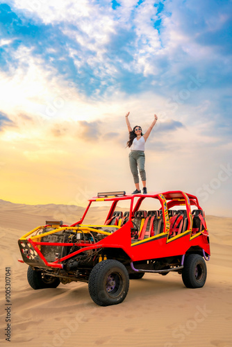 Obraz na plátně Young woman celebrating on top of a colorful dune buggy in the Huacachina desert, Ica, Peru, enjoying the sunset and adventure