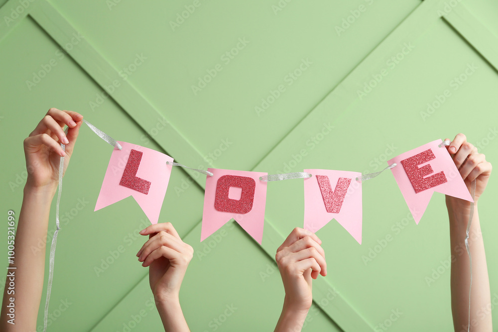 Obraz premium Women holding paper flags with word LOVE against color wall, closeup. Valentine's Day celebration