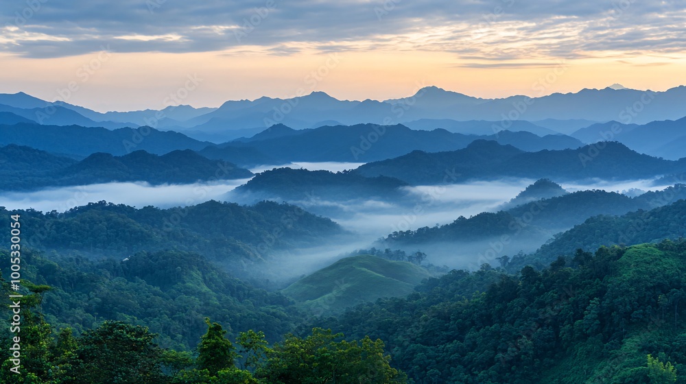 Obraz premium Serene sunrise over misty mountain ranges with layers of blue clouds and lush green valleys.