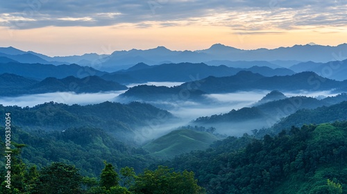 Serene sunrise over misty mountain ranges with layers of blue clouds and lush green valleys.