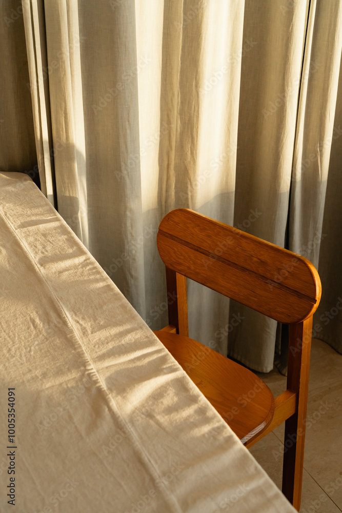 A sunlit wooden chair beside a softly draped table in a cozy room with curtains illuminated by warm afternoon light A sunlit wooden chair beside a softly draped table in a cozy room with curtains illuminated by warm afternoon light