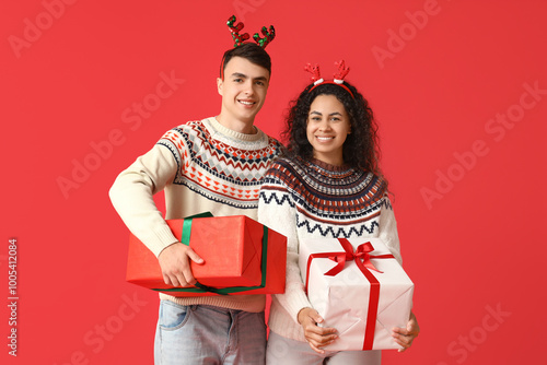 Happy young couple in festive sweaters and reindeer antlers holding christmas...