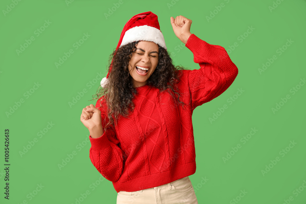 Beautiful young African-American woman in Santa hat on green background. Christmas celebration Beautiful young African-American woman in Santa hat on green background. Christmas celebration