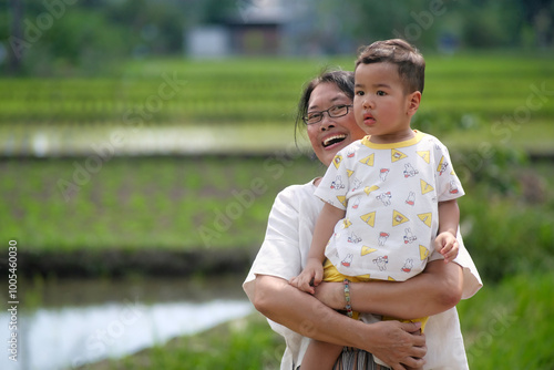 Grandma carrying her two-year-old grandson walking around rice field in the village photo