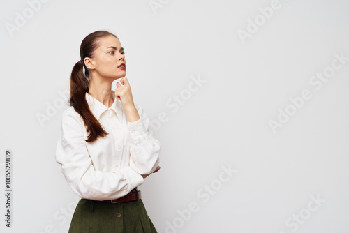 thoughtful woman in white shirt, pondering expression, standing against simple gray background, arms crossed, confidence, youthful appearance, modern style, professional look, engagement