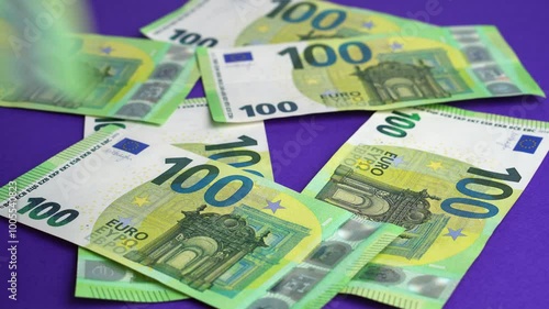 Money falling on table. Dropping lot of one hundred Euro paper banknotes on purple background