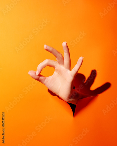 Woman's hand shows ok sign through orange background
