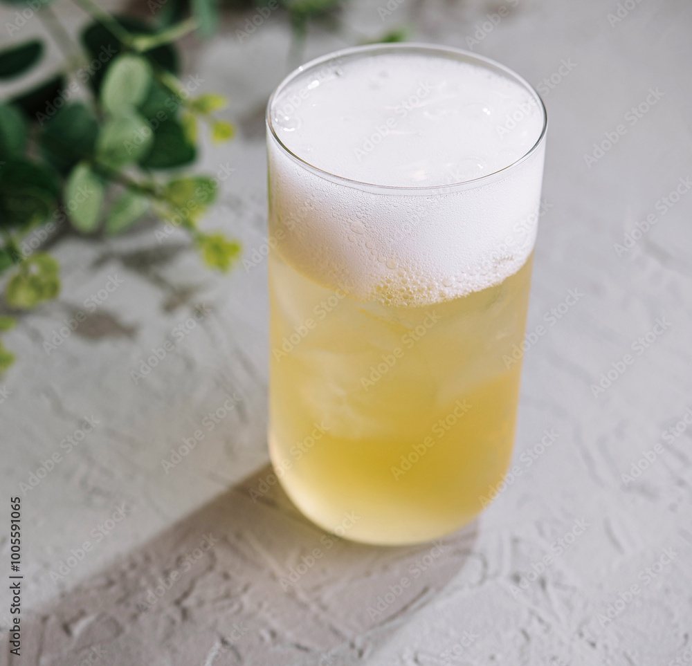 Glass of cold cocktail with foam on white table background with green leaves Glass of cold cocktail with foam on white table background with green leaves