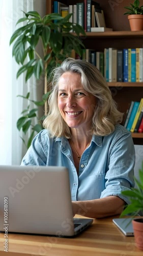 A woman is sitting at a desk with a laptop in front of her. She is smiling and she is happy