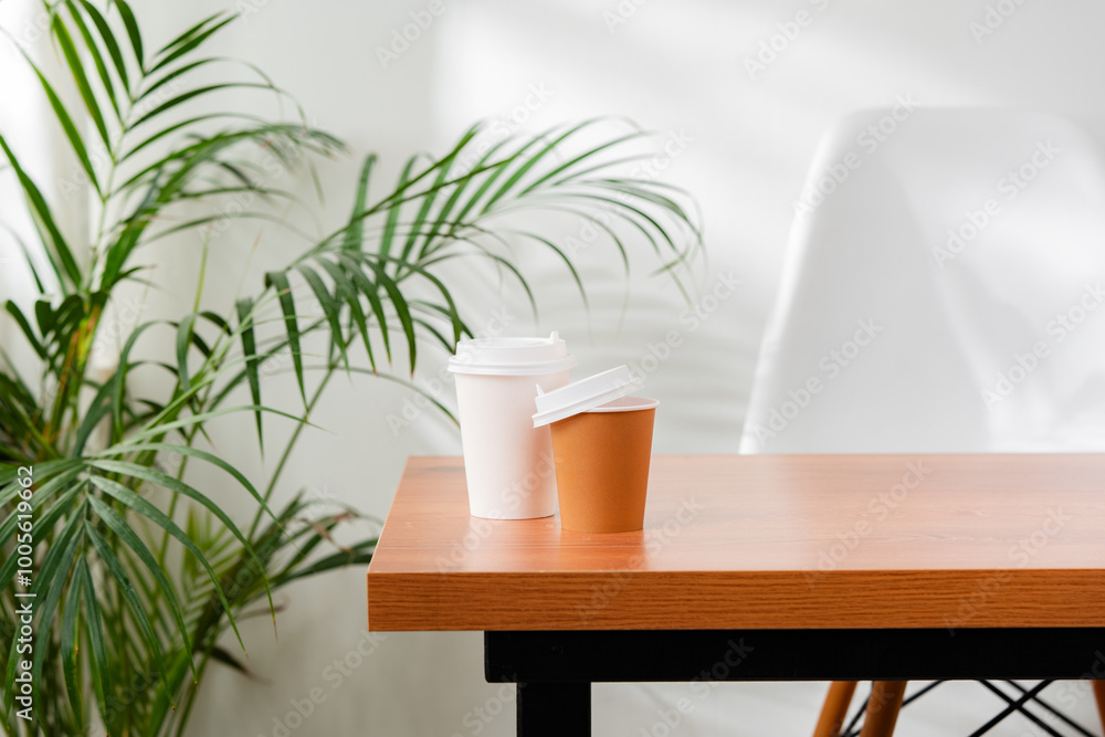 A disposable coffee cup on a wooden table beside a leafy plant A disposable coffee cup on a wooden table beside a leafy plant