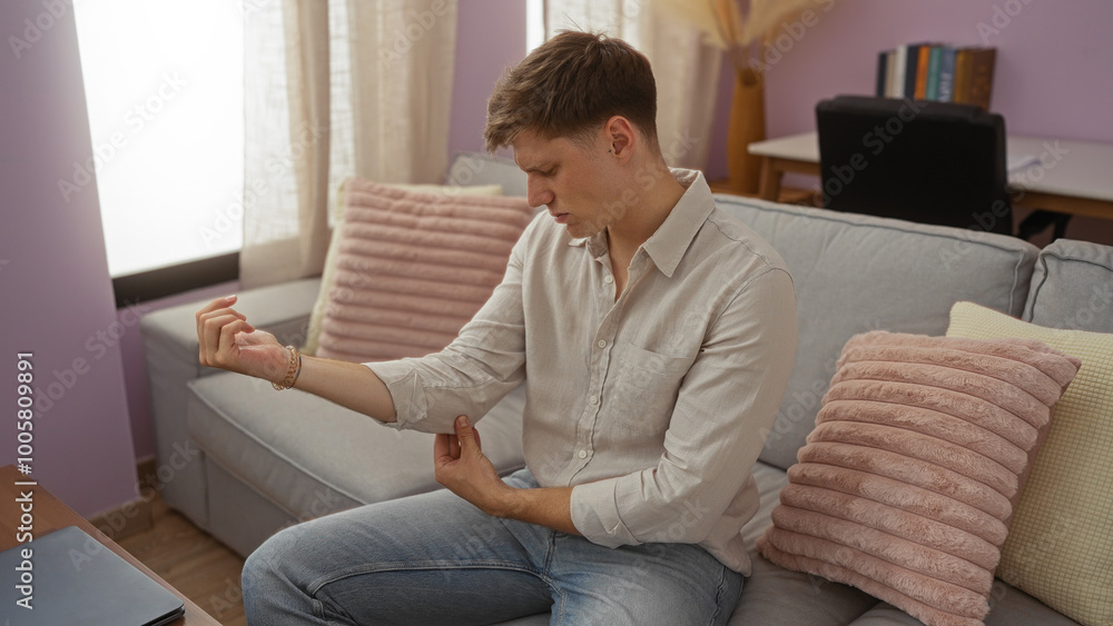 Young man in a living room holding his elbow and seeming to be in discomfort, surrounded by cozy interior elements like a couch and cushions Young man in a living room holding his elbow and seeming to be in discomfort, surrounded by cozy interior elements like a couch and cushions