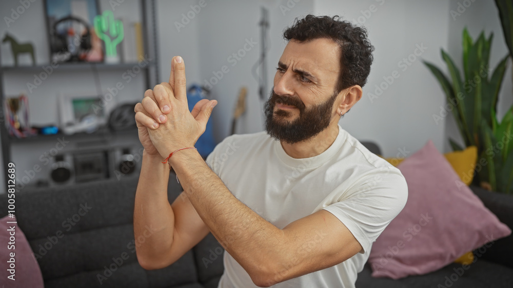 Bearded man makes gun gesture indoors, with modern decor and plants in living room background. Bearded man makes gun gesture indoors, with modern decor and plants in living room background.