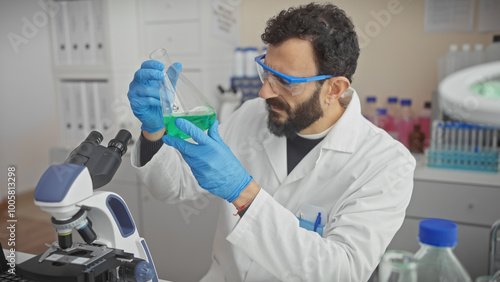 A bearded man in lab coat examines a flask in a laboratory setting with precision equipment around, showcasing scientific research.