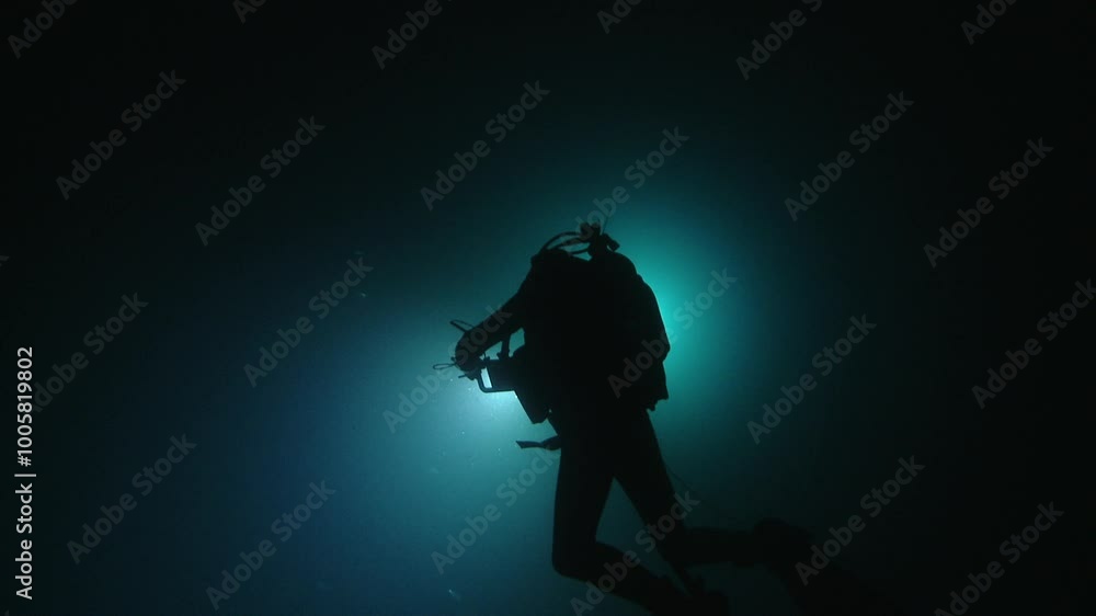 A diver illuminated from behind, creating a silhouette against the dark ocean depths, showcasing the mysterious beauty of the underwater world. Check my portfolio for more ocean footage. A diver illuminated from behind, creating a silhouette against the dark ocean depths, showcasing the mysterious beauty of the underwater world. Check my portfolio for more ocean footage.
