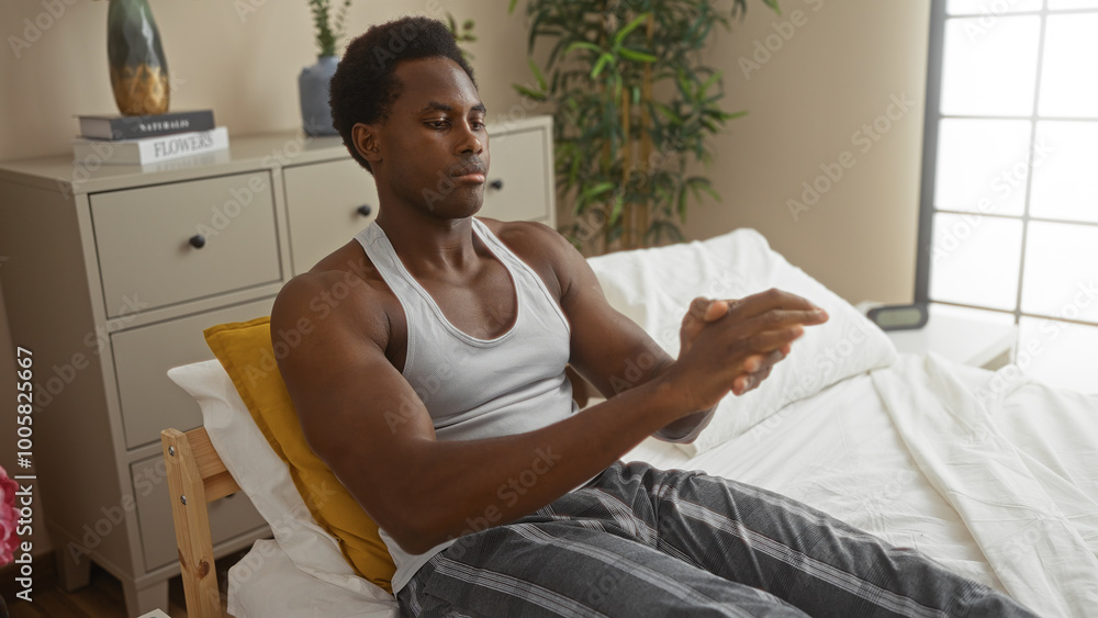 Fototapeta premium Young man applying cream on his hands while sitting on a bed in a cozy bedroom