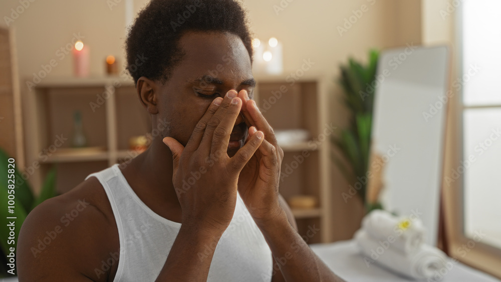 Handsome young african american man relaxing in a spa wellness center with candles and greenery in the background Handsome young african american man relaxing in a spa wellness center with candles and greenery in the background