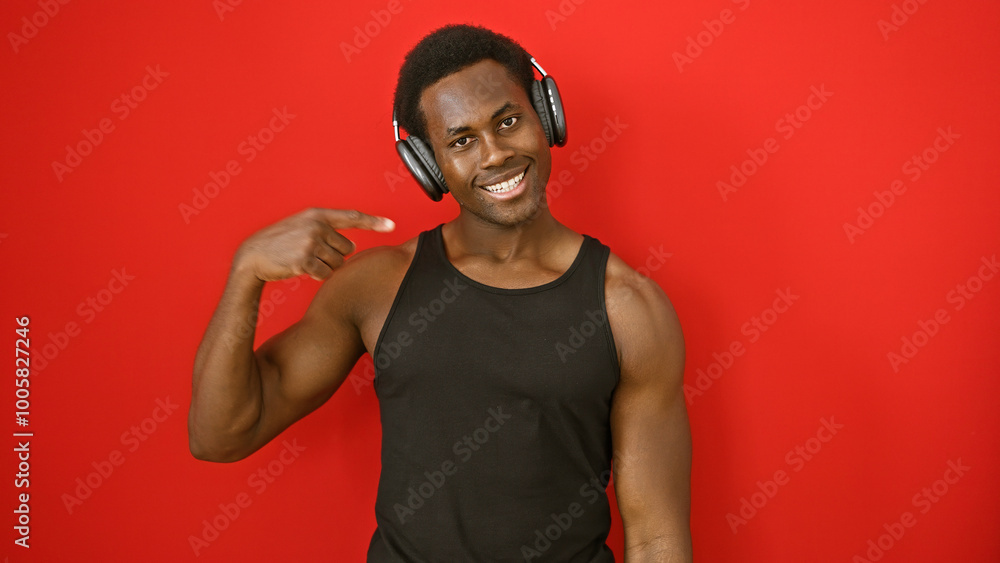 A smiling young african american man points to himself while wearing headphones against a red background. A smiling young african american man points to himself while wearing headphones against a red background.