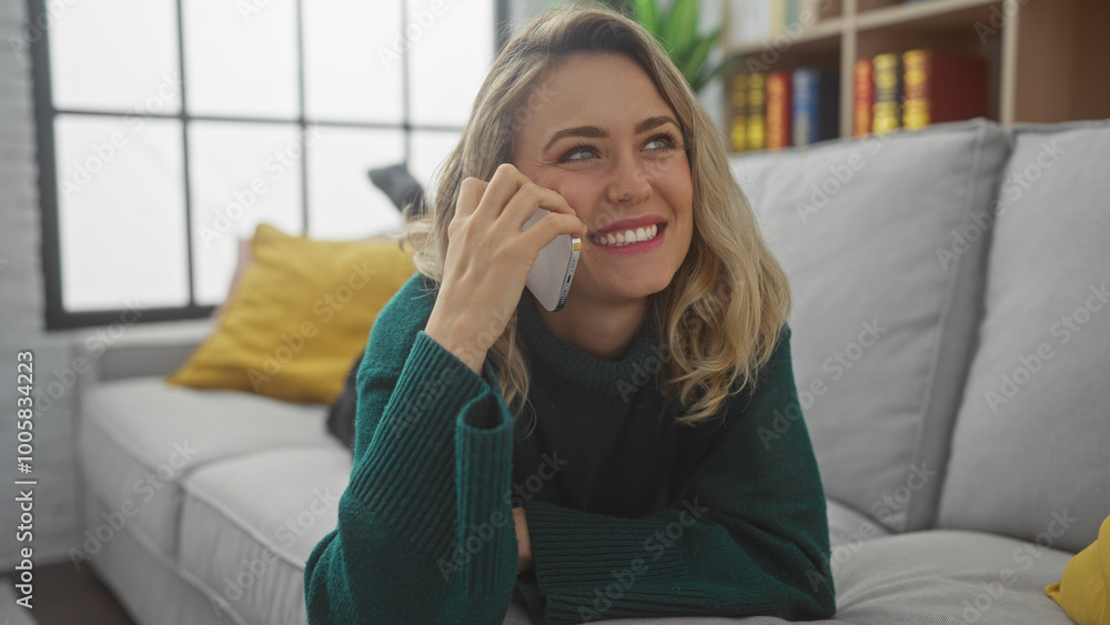 Smiling blonde woman chatting on a smartphone in a cozy living room setting, exuding a casual, relaxed atmosphere. Smiling blonde woman chatting on a smartphone in a cozy living room setting, exuding a casual, relaxed atmosphere.