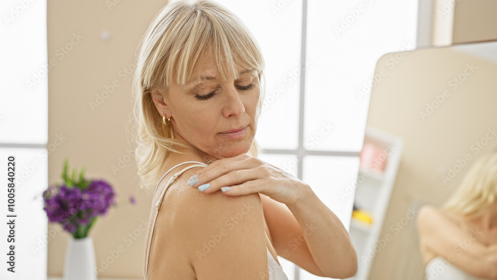 A middle-aged blonde woman applies lotion while in a well-lit, modern bathroom at home. A middle-aged blonde woman applies lotion while in a well-lit, modern bathroom at home.