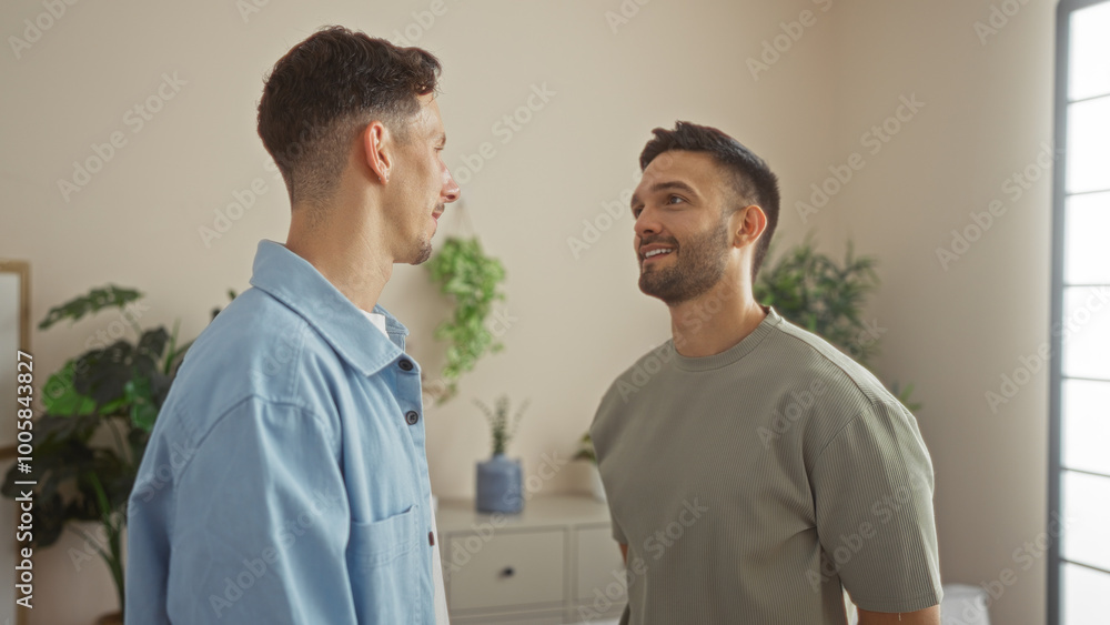 Fototapeta premium Men couple standing together in a cozy living room, showcasing love and connection in a modern home with indoor plants, highlighting an intimate lgbtq family scene.