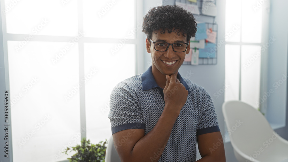 Fototapeta premium Young man smiling in a bright office, creating a positive and welcoming environment in a professional workspace with modern decor and natural light.