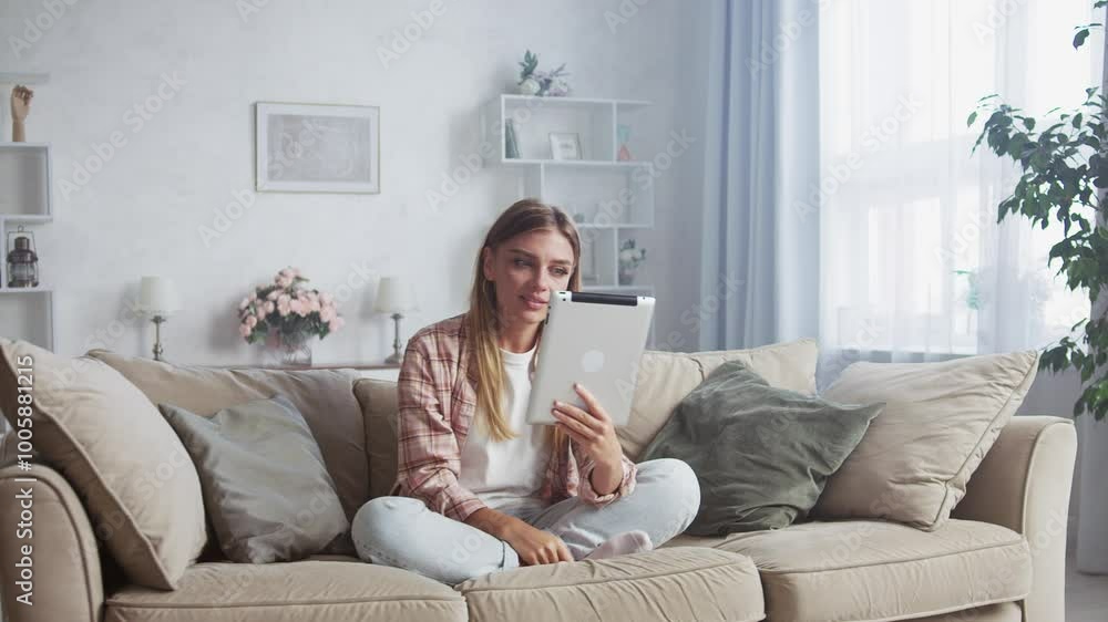 Young woman is sitting on a sofa in her living room, using a tablet. She experiences a range of emotions, from happiness to surprise Young woman is sitting on a sofa in her living room, using a tablet. She experiences a range of emotions, from happiness to surprise