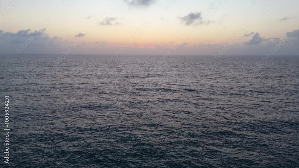A drone flies over the ocean surface at sunrise in slow motion. Clouds rise on the horizon, with deep blue, orange, and light blue tones. The camera captures waves from different angles. A drone flies over the ocean surface at sunrise in slow motion. Clouds rise on the horizon, with deep blue, orange, and light blue tones. The camera captures waves from different angles.