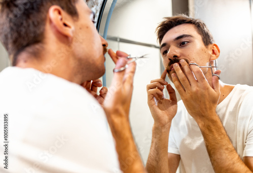 Foto Young man trims his mustache with scissors in the bathroom in front of the mirror
