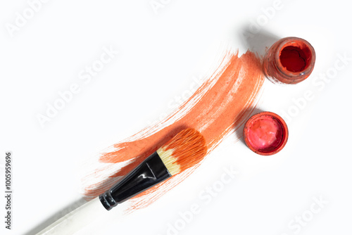 Vibrant red paint stroke on white background, paint brush above and red paint bottle on side.