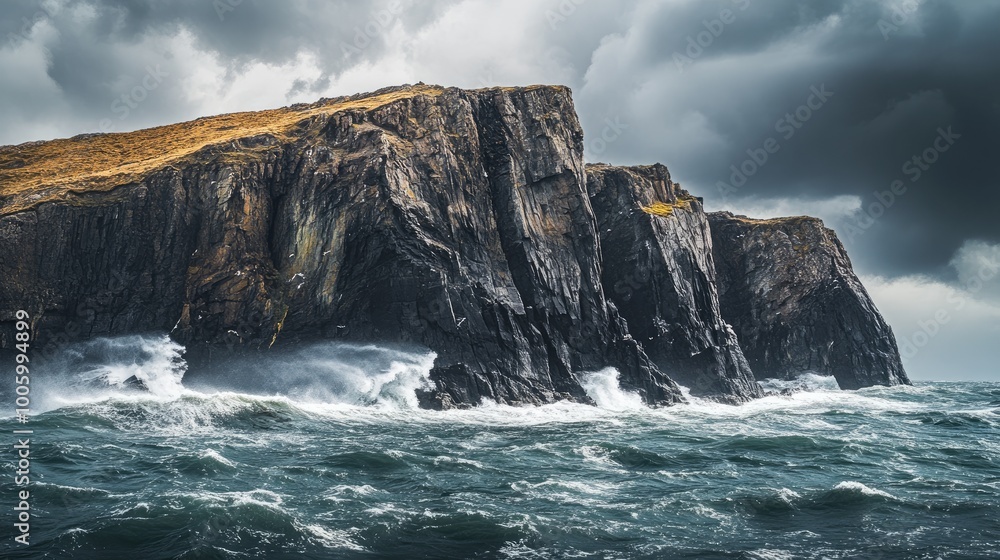 Fototapeta premium A rocky island with steep cliffs rising from the ocean, surrounded by rough waves and stormy skies.