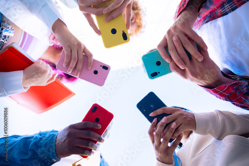 Low-angle shot of a group of diverse hands holding brightly colored smartphones, forming a circle. The photo showcases modern communication and social media interaction in a vibrant, connected setting