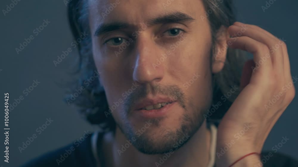 a young man with long hair with large expressive eyes, European appearance, looks incredulously into the frame, his mouth is covered with his hand, he shakes his head negatively, he leans on his hand a young man with long hair with large expressive eyes, European appearance, looks incredulously into the frame, his mouth is covered with his hand, he shakes his head negatively, he leans on his hand
