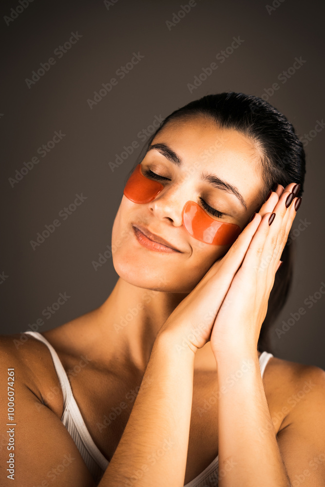 Naklejka premium Young woman with perfect glowing skin and natural makeup posing for the camera with medical collagen patches under her eyes to reduce fatigue and puffiness. Skin care.Modern beauty tools concept