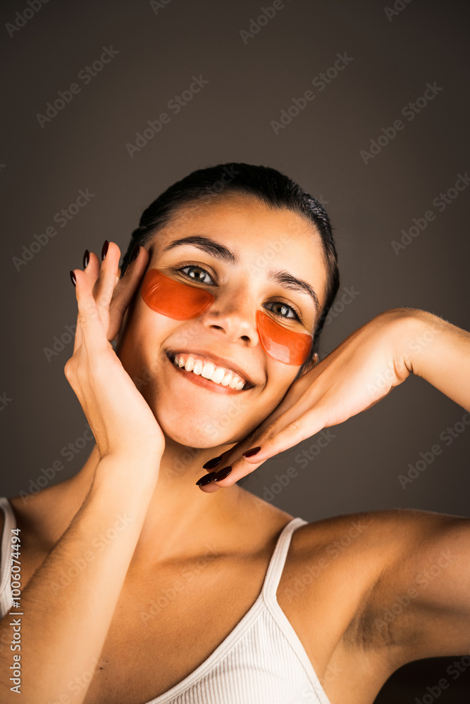 Fototapeta premium Young woman with perfect glowing skin and natural makeup posing for the camera with medical collagen patches under her eyes to reduce fatigue and puffiness. Skin care.Modern beauty tools concept