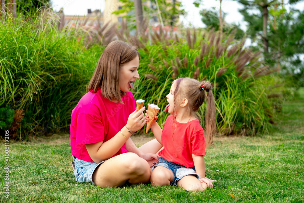 Obraz premium mom and daughter eat ice cream in the summer on the green lawn and enjoy having fun and weekends together, a happy family on vacation, a mother with a small child walking in the summer