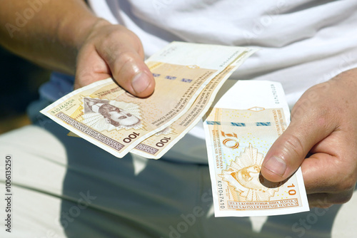 A tourist paying in cash during his holiday in Bosnia and Herzegovina: a man holds out a 10 Bosnian convertible mark note and in his other hand holds two more 100 BAM (KM) notes, close-up photo.