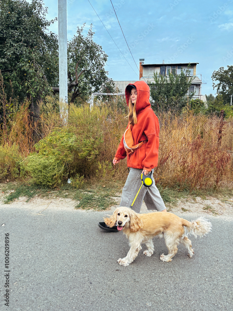 irl in a red hoodie walking her dog in a serene outdoor setting. Lifestyle shot emphasizing daily routines, pet care, and relaxed casual fashion. Ideal for animal and outdoor themes. Vertical photo