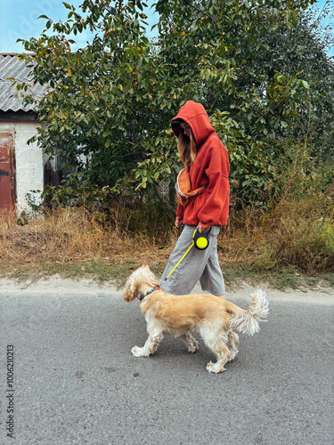 Obraz na płótnie Side view of a woman walking her dog on a leash in casual attire. Streetwear fashion and outdoor lifestyle with a focus on pet care, ideal for content related to pets, health, or fashion. w salonie
