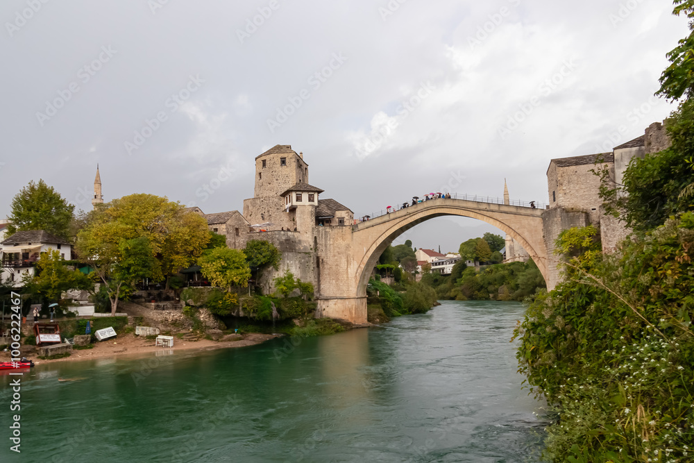 Scenic view of Old Bridge of medieval town Mostar spanning the Neretva River, Bosnia and Herzegovina. UNESCO World Heritage Site in. Ancient arch stone structure at cloudy day surrounded by minarets Scenic view of Old Bridge of medieval town Mostar spanning the Neretva River, Bosnia and Herzegovina. UNESCO World Heritage Site in. Ancient arch stone structure at cloudy day surrounded by minarets