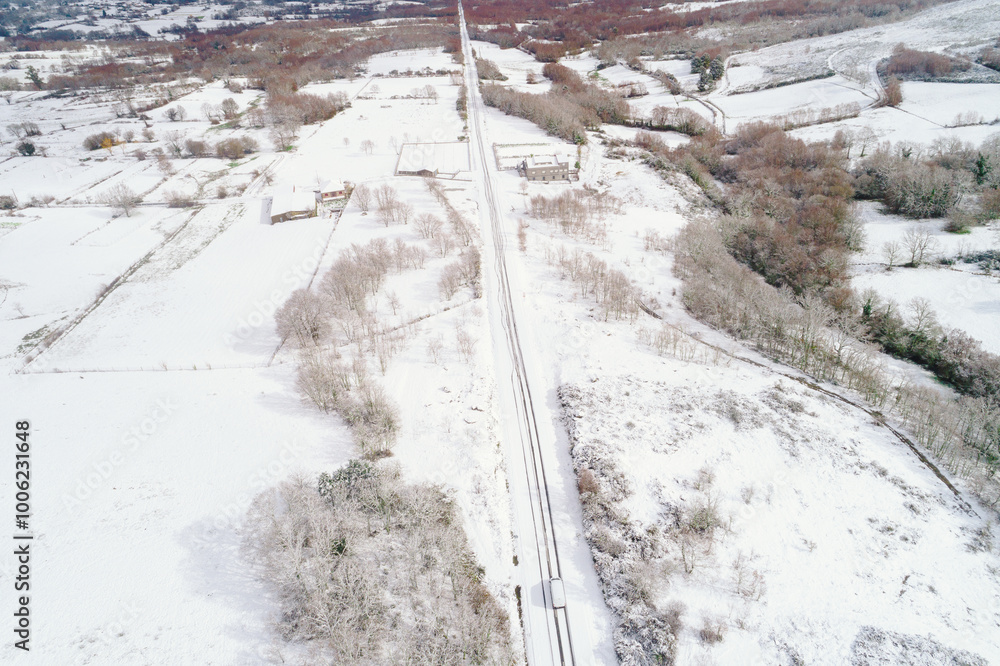 snowy landscape and a snow-covered road in winter, with a vehicle driving. Aerial view with drone snowy landscape and a snow-covered road in winter, with a vehicle driving. Aerial view with drone