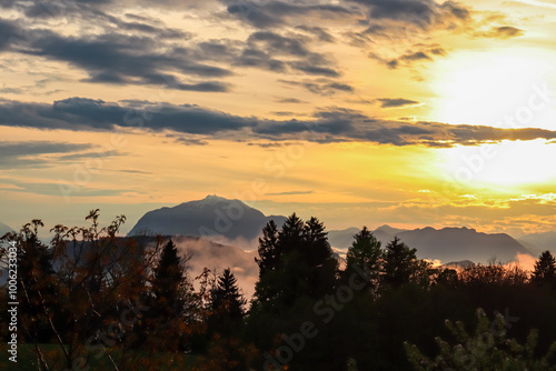 Fiery sunset over mountain summit Dobratsch in Rosental, Carinthia, Austria, Europe. Silhouette of forest and rolling hills in Austrian Alps. Vibrant orange and yellow hues. Tranquil serene atmosphere photo