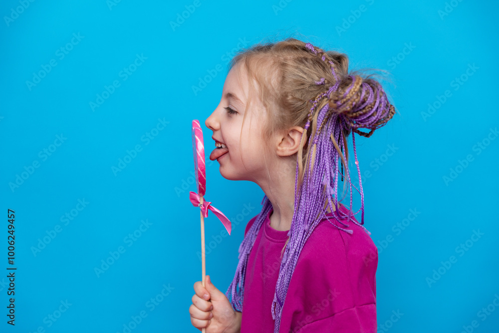 Happiness, childhood, kid and sweets. Side view little girl holding a heart shaped lollipop caramel on a stick, A festive candy in the hands of child in pink t-shirt on blue background. Valentines Day Happiness, childhood, kid and sweets. Side view little girl holding a heart shaped lollipop caramel on a stick, A festive candy in the hands of child in pink t-shirt on blue background. Valentines Day