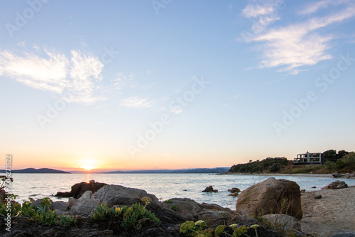 View through rocks on a sandy beach into the sunset. Landscape shot with a view to the horizon over the wide sea on the coast of Ouranoupoli, Thessaloniki, Central Macedonia, Greece photo