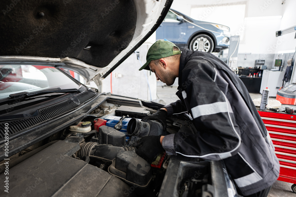 A focused mechanic inspects a car engine in a modern auto repair shop. The garage has tools and equipment, highlighting professionalism and technical expertise in vehicle maintenance. A focused mechanic inspects a car engine in a modern auto repair shop. The garage has tools and equipment, highlighting professionalism and technical expertise in vehicle maintenance.